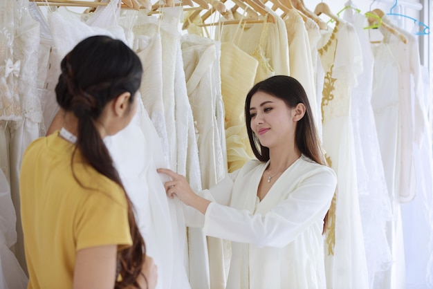 Smiling customer holding wedding dresses by tailor in bridal shop