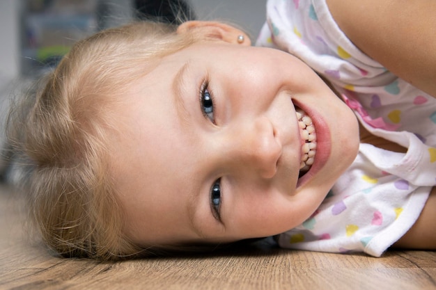 Smiling cute beautiful child girl in tshirt lying on wooden floor