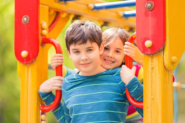 Улыбающиеся милые брюнетки мальчика и девочки стоят среди желтой красочной детской площадки
