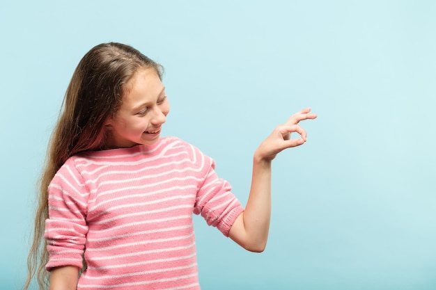 Smiling cute girl holding virtual object on invisible string in hands empty space for product placement