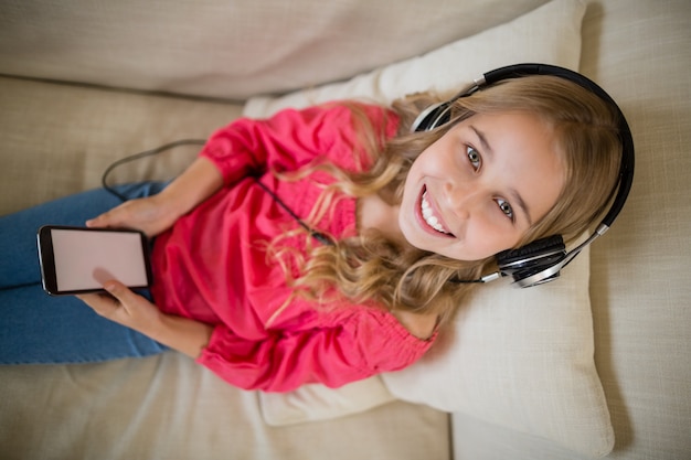 집에서 거실에서 헤드폰으로 음악을 듣고 웃는 귀여운 소녀