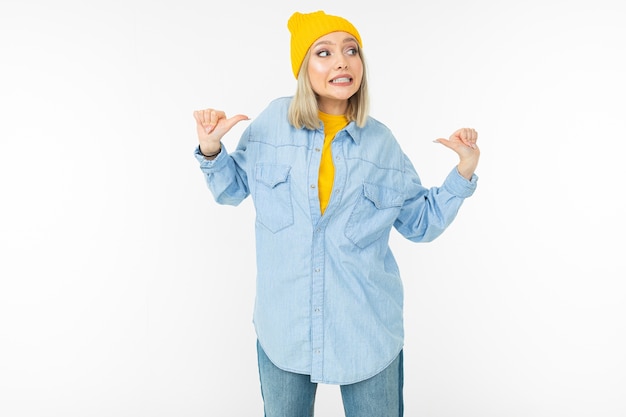 Smiling cute girl in a stylish denim shirt and a yellow hat shows like on a white studio background.