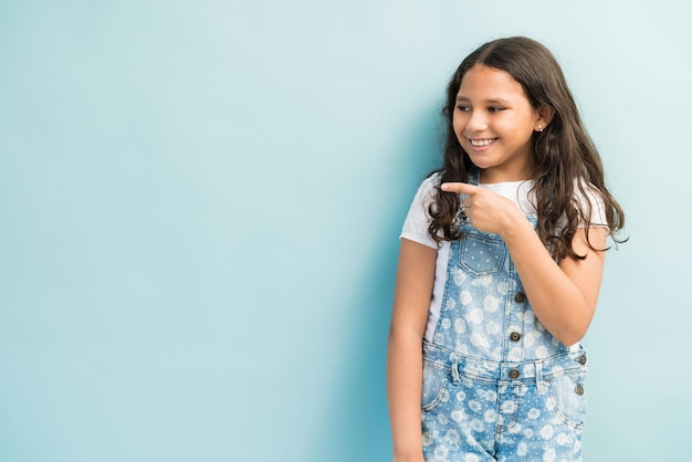 Smiling cute Latin girl pointing while looking away in studio