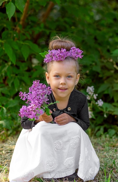 頭にライラックの花輪と5歳のかわいい小さな女の子の子供の子供を笑顔