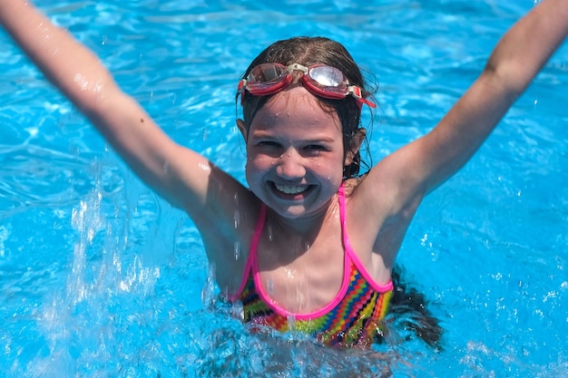 Smiling cute little girl in goggles in swimming pool on sunny summer day