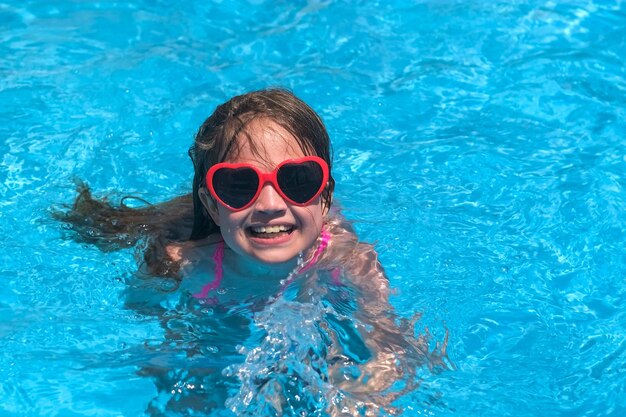 Photo smiling cute little girl in heart shaped sunglasses in swimming pool on sunny day