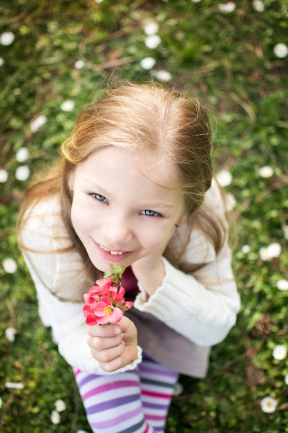 花を持ってカメラを見て春の牧草地でかわいい女の子の笑顔。