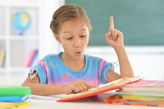 Smiling cute little girl reading book at classroom