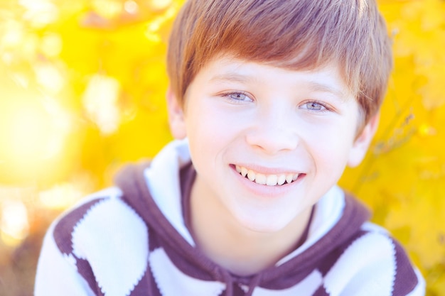 Smiling cute teen kid boy with yellow autumn fallen leaves outdoor in park. Fall season
