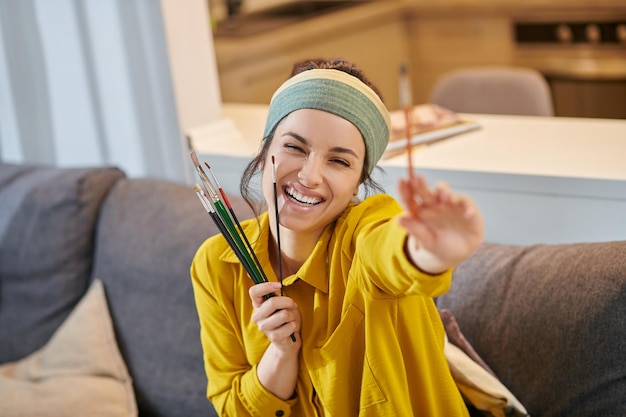 Smiling cute young woman with a palette and brushes in\
hands