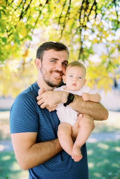 Smiling dad holds a baby in his arms hugging him Portrait