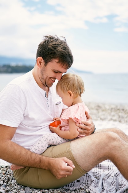 Smiling dad holds a little girl in his arms on a pebble beach