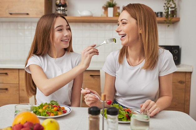 Smiling daughter feeding joyful mother with salad