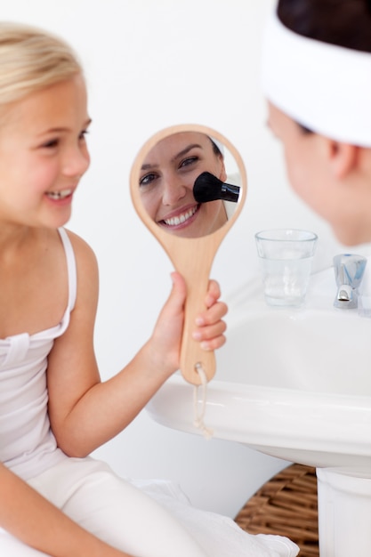 Smiling daughter holding a mirror and mother putting makeup