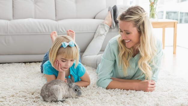 Smiling daughter and mother laying on the floor with rabbit