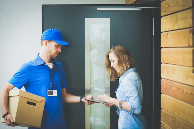 Photo smiling delivery man in blue uniform delivering parcel box to recipient courier service concept smiling delivery man in blue uniform