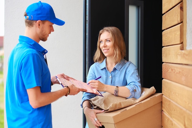Uomo di consegna sorridente in uniforme blu che consegna la scatola dei pacchi al concetto di servizio di corriere del destinatario uomo di consegna sorridente in uniforme blu