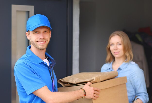 Smiling delivery man in blue uniform delivering parcel box to recipient courier service concept Smiling delivery man in blue uniform