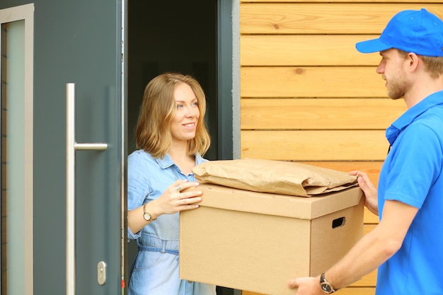 Smiling delivery man in blue uniform delivering parcel box to recipient courier service concept Smiling delivery man in blue uniform