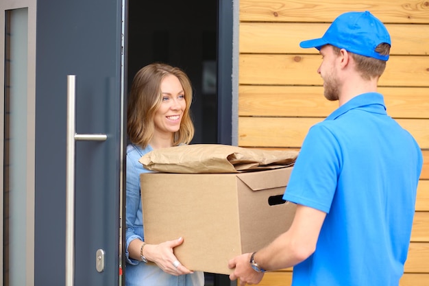 Smiling delivery man in blue uniform delivering parcel box to recipient courier service concept Smiling delivery man in blue uniform