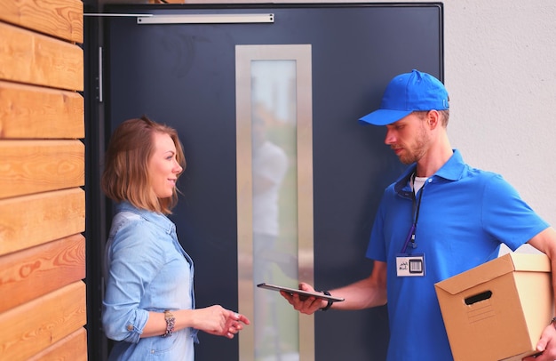 青い制服を着た笑顔の配達人が宅配ボックスを受取人に配達します 宅配便サービスのコンセプト 青い制服を着た笑顔の配達人