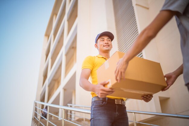 写真 笑顔の配達員が街の建物で顧客に荷物を渡している