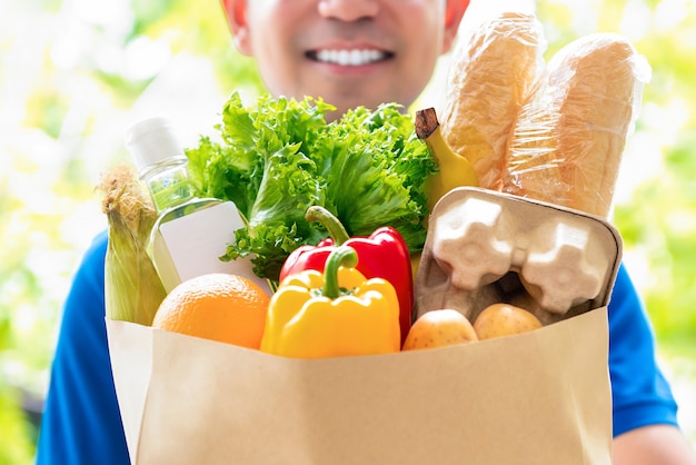 Smiling delivery man holding a grocery bag ready to deliver to the customer at home