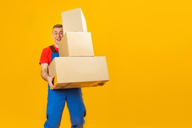 Smiling delivery man or loader holds cartboard boxes on yellow background in studio copy space mock up