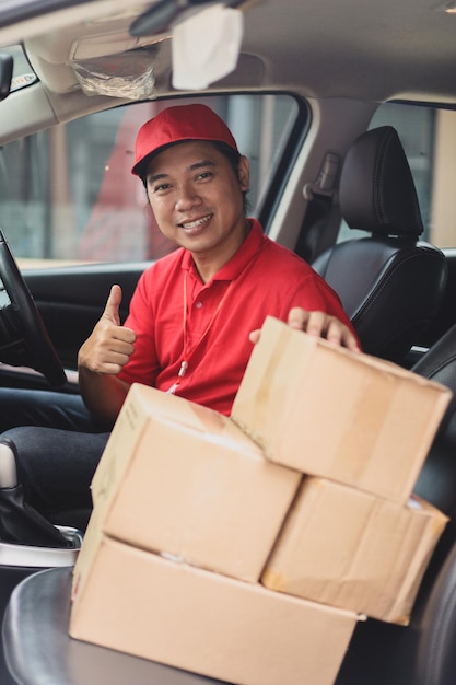 Smiling delivery man showing thumb up sitting with pile of cardboard in delivery van.