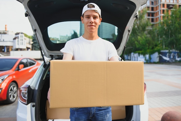 Photo smiling delivery man standing in front of his car