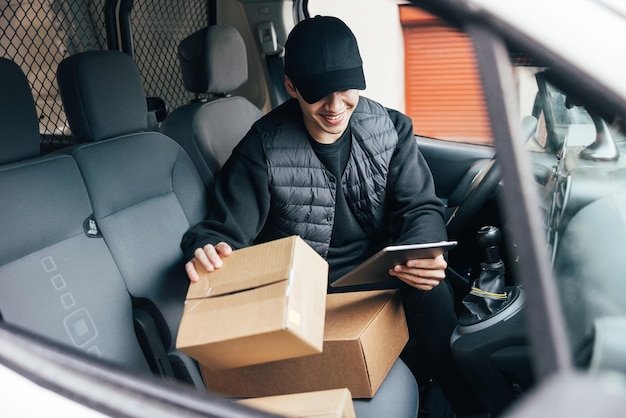 車に乗っている荷物を持った笑顔の配達人