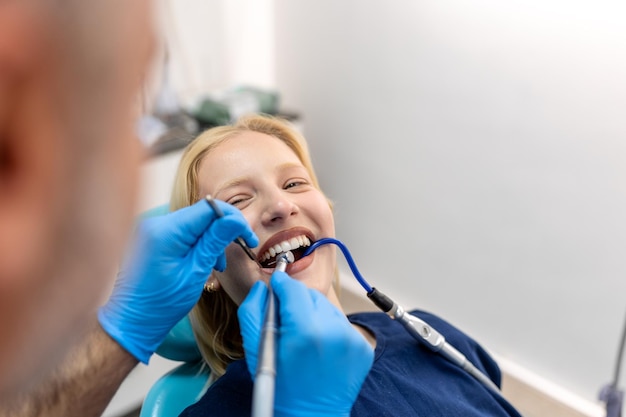 Dentista sorridente che comunica con la giovane donna mentre controlla i suoi denti durante la procedura dentale presso l'ufficio del dentista