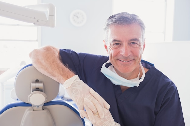 smiling dentist leaning against dentists chair 