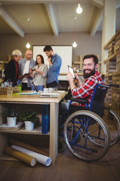 Uomo d'affari disabile sorridente che per mezzo della compressa digitale