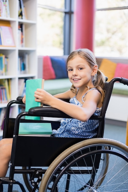 Улыбается инвалид школьница на инвалидной коляске держит книги в библиотеке