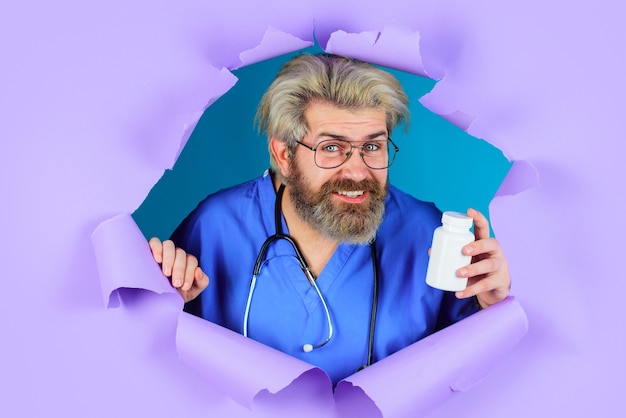 Smiling doctor breaking through the purple background holding a bottle of pills