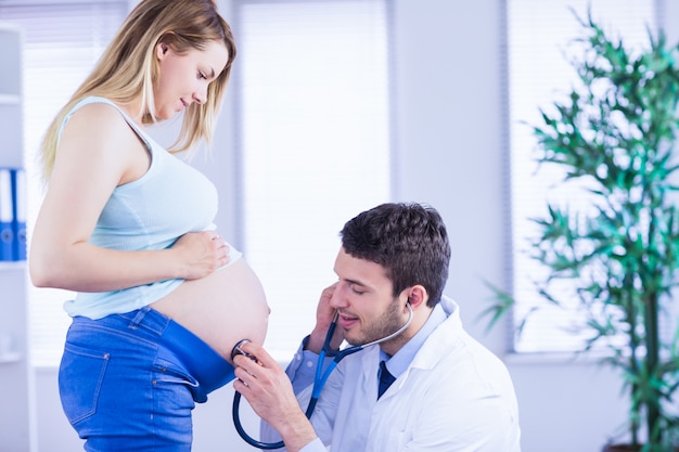 Smiling doctor examining stomach of standing pregnant patient 