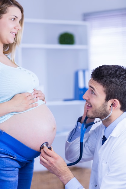 立っている妊娠している患者の胃を調べている笑い医師