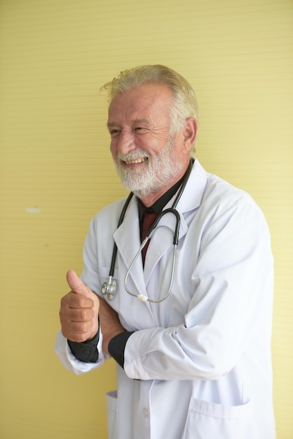 Photo smiling doctor showing thumbs up sign by wall at hospital