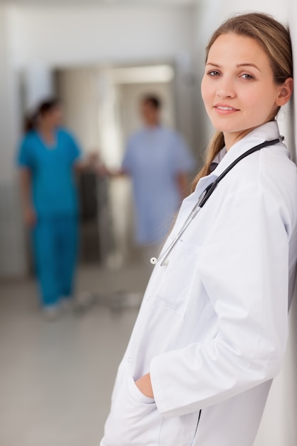 Smiling doctor standing against a wall with her hands in her pockets