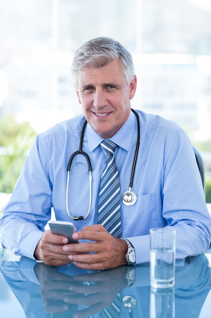 Smiling doctor texting with his mobile phone