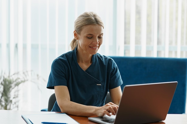 Smiling doctor therapist working laptop during appointment in her medical office