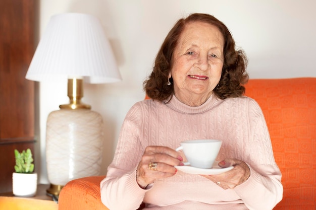 Donna caucasica anziana sorridente che beve caffè o tè a casa