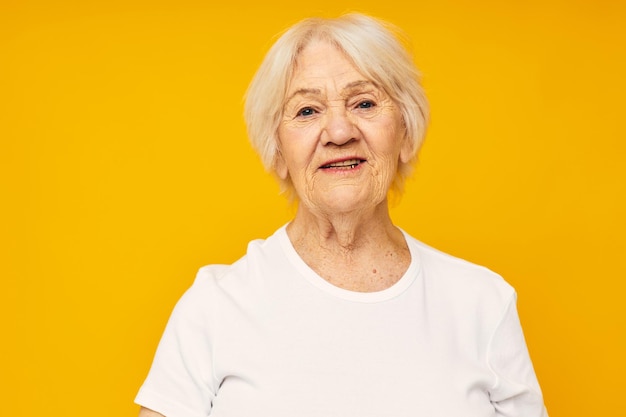 Smiling elderly woman in casual tshirt gestures with his hands yellow background