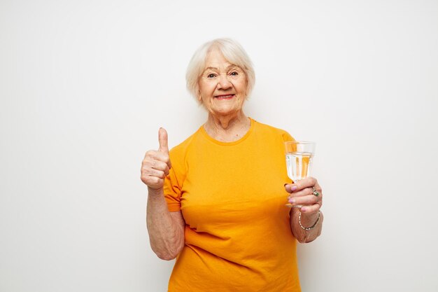 Smiling elderly woman in casual tshirt glasses glass of water isolated background