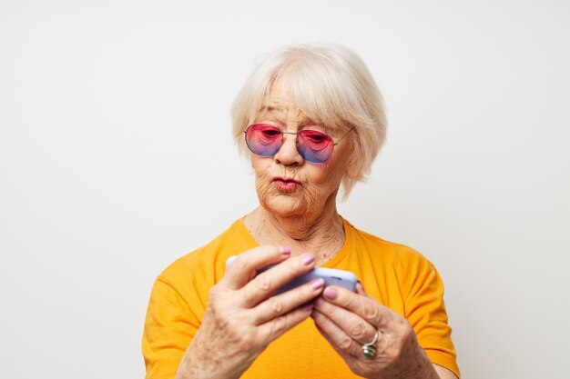 Smiling elderly woman in fashionable glasses with a smartphone in hand cropped view