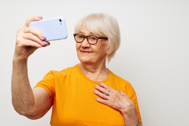 手で分離された背景のスマートフォンとファッショナブルなメガネで笑顔の年配の女性