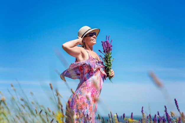 Smiling elderly woman in a hat and sundress in a field with a purple sage bouquet leisure vacation and relaxation