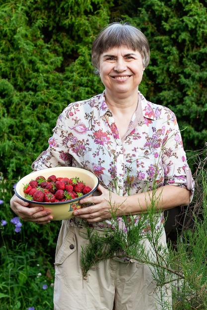 Smiling elderly woman holding a bowl of fresh strawberries in her hands