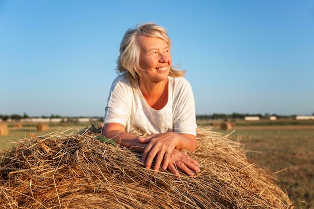 笑顔の年配の女性が日没の野原の干し草の山に横たわっているアクティブなライフスタイルの健康と自然